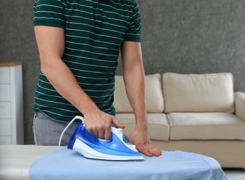 Photo of Man ironing shirt on board at home, closeup. Space for text