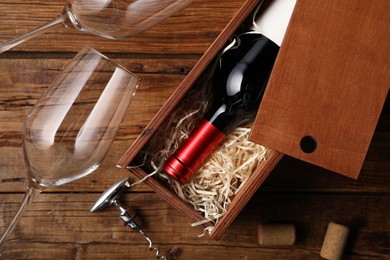 Photo of Box with wine bottle, glasses, corkscrew and corks on wooden table, flat lay