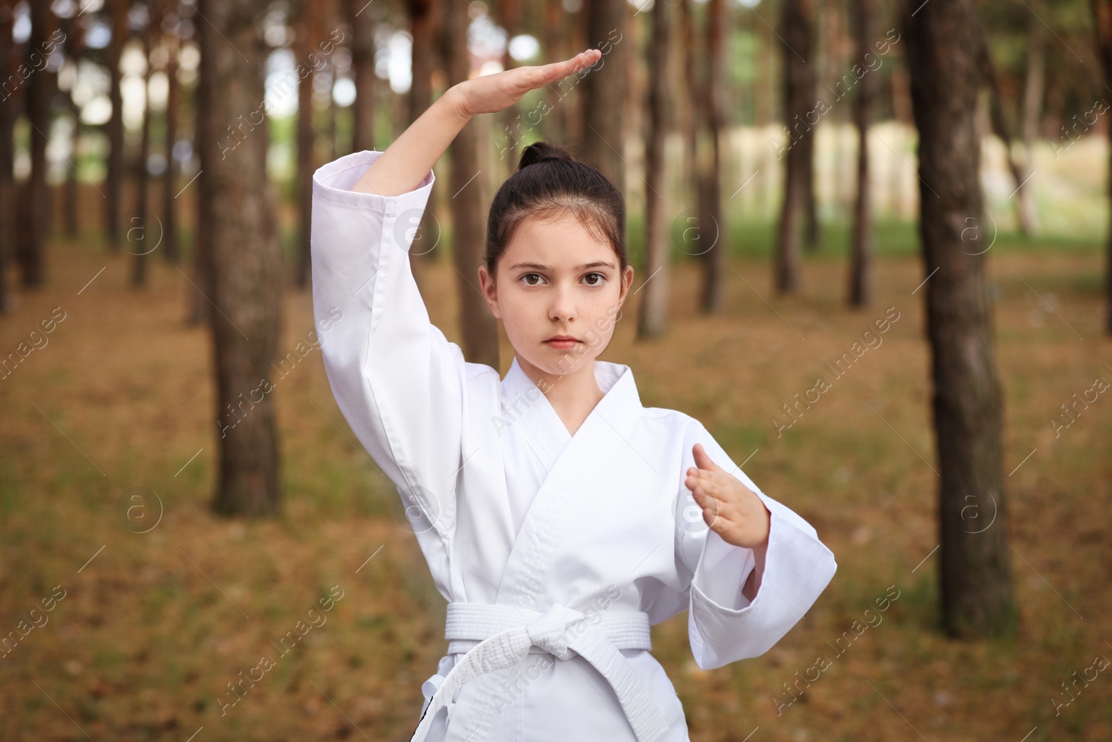 Photo of Cute little girl in kimono practicing karate in forest