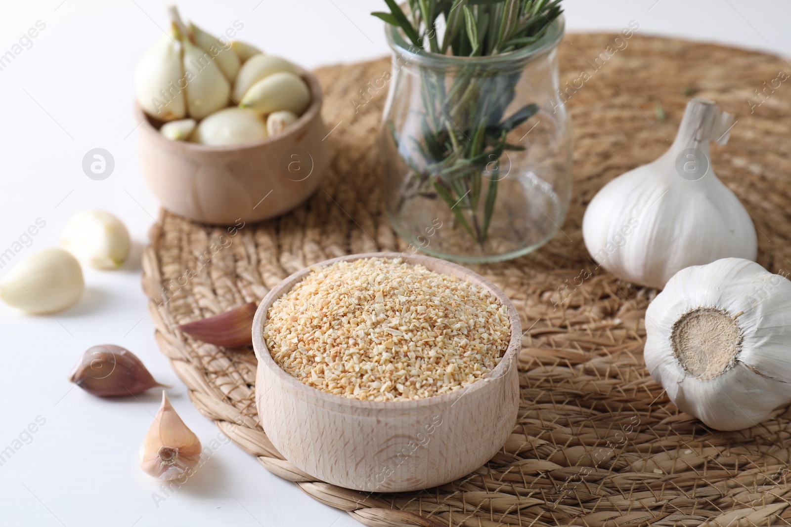 Photo of Dehydrated garlic granules in bowl, fresh bulbs and cloves on white table