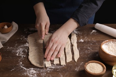 Photo of Woman cutting dough at wooden table, closeup. Cooking grissini