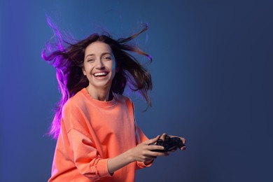 Emotional woman with game controller on dark blue background