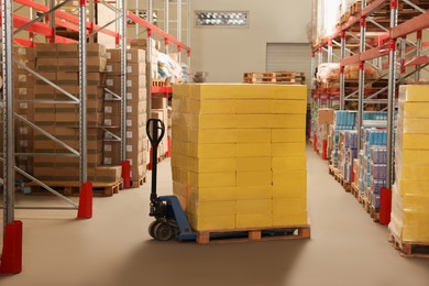 Photo of Manual pallet truck with stacked boxes in warehouse. Wholesaling