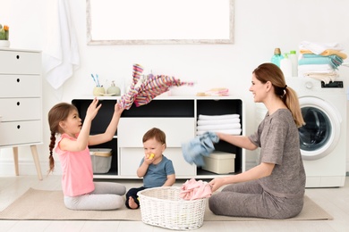 Photo of Housewife and children having fun while folding freshly washed clothes in laundry room