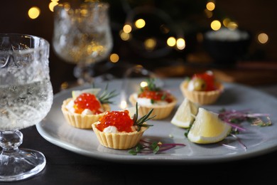 Delicious tartlets with red caviar served on black table against blurred festive lights, closeup. Space for text