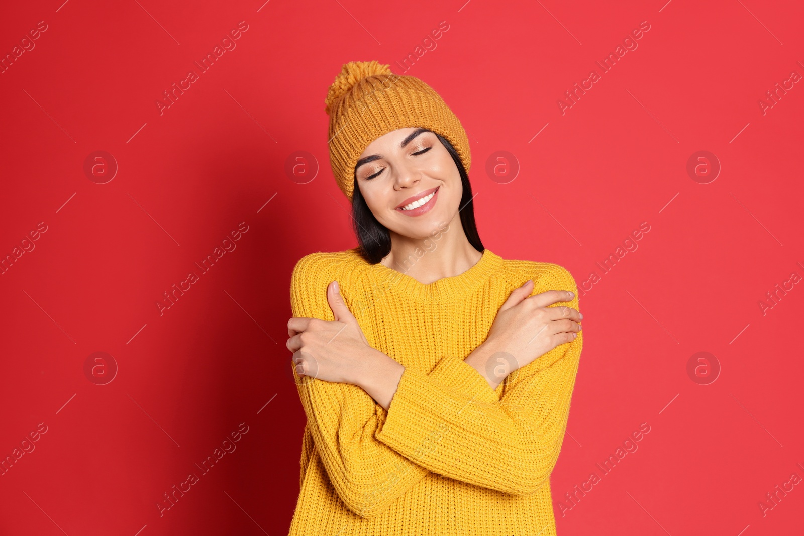Photo of Young woman wearing warm sweater and hat on red background. Winter season