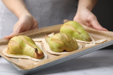 Woman holding tray of pastries with dough and fresh pears at white table, closeup