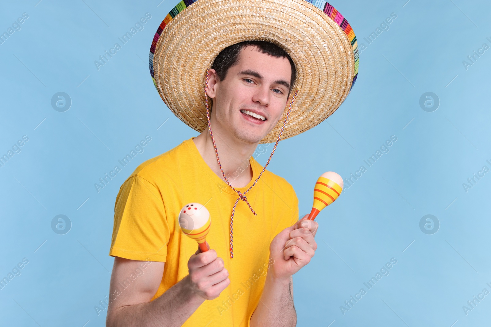 Photo of Young man in Mexican sombrero hat with maracas on light blue background