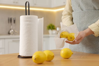 Photo of Woman wiping lemons with paper towels in kitchen, closeup