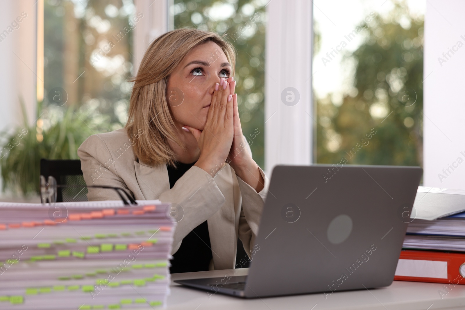 Photo of Overwhelmed woman sitting at table with stacks of documents and folders in office