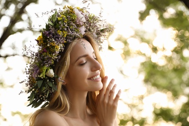 Young woman wearing wreath made of beautiful flowers outdoors on sunny day