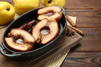 Tasty baked quinces with spices and honey in dish on wooden table. Space for text