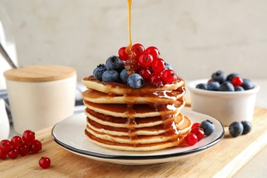 Pouring syrup onto pancakes with fresh berries on table