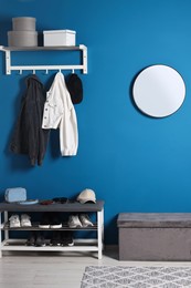 Photo of Stylish hallway with shoe storage bench and ottoman near blue wall. Interior design