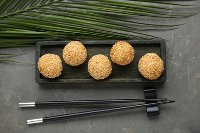 Delicious sesame balls, green leaf and chopsticks on grey table, flat lay