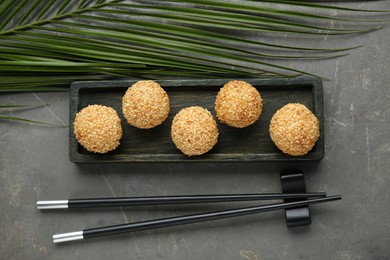 Photo of Delicious sesame balls, green leaf and chopsticks on grey table, flat lay