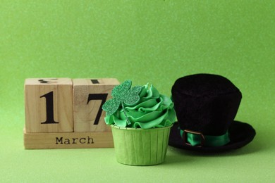 Photo of St. Patrick's day party. Tasty cupcake with clover leaf topper, leprechaun hat and wooden block calendar on green background