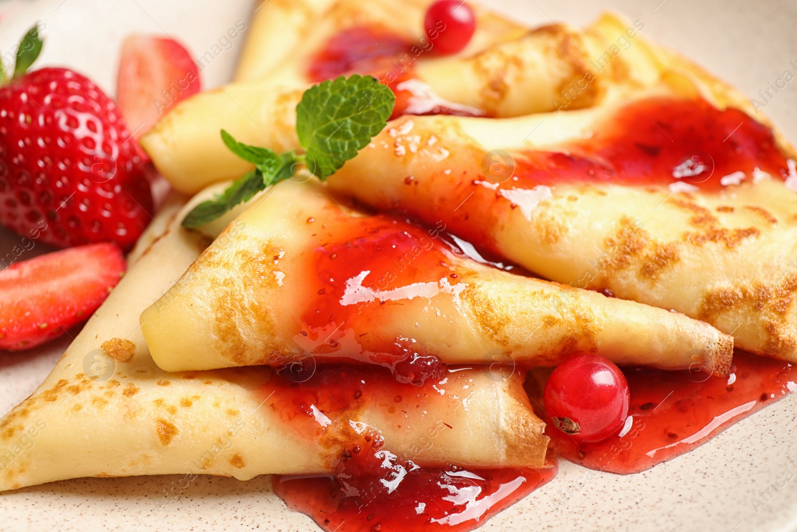 Photo of Delicious thin pancakes with strawberries and jam, closeup