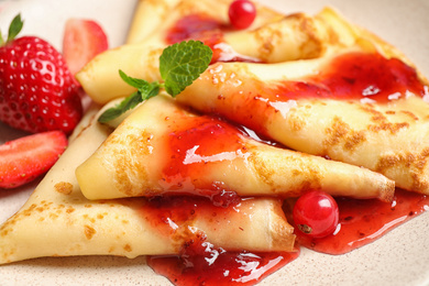 Delicious thin pancakes with strawberries and jam, closeup