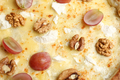 Delicious cheese pizza with walnuts and grapes as background, closeup