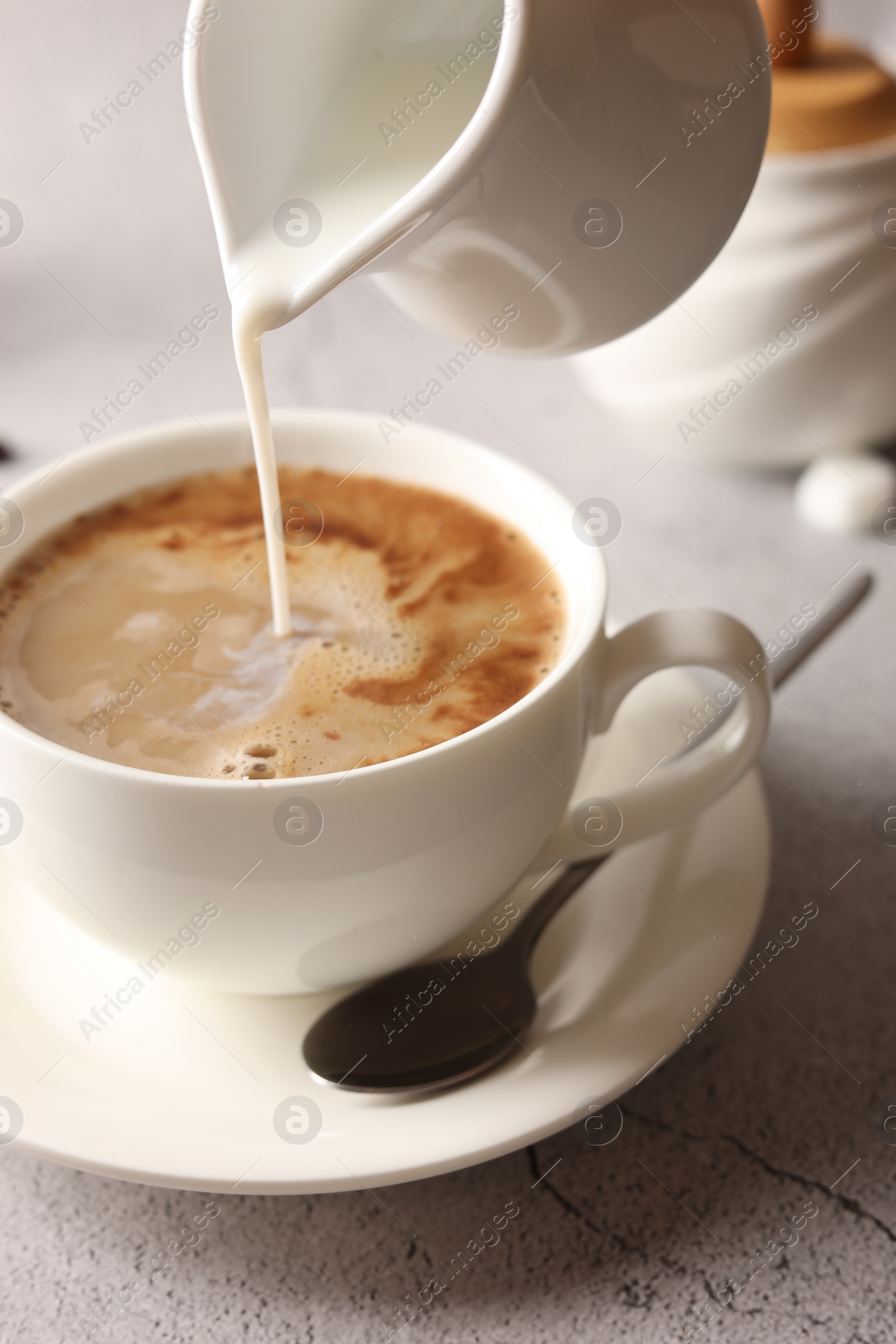 Photo of Pouring milk into cup with coffee on light grey textured table, closeup