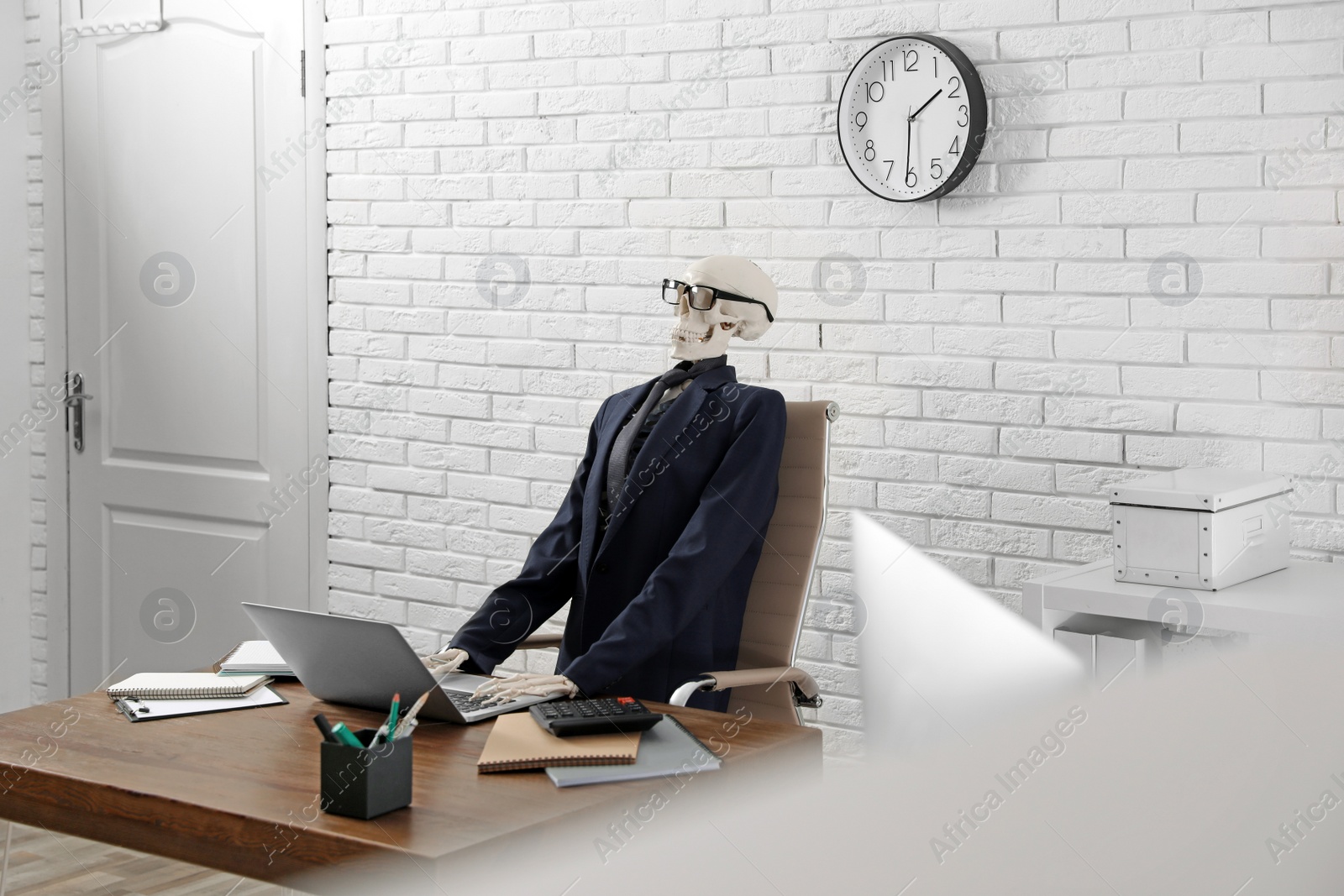 Photo of Human skeleton in suit using laptop at table in office