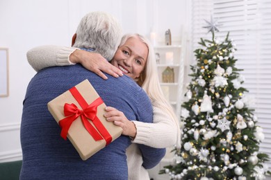 Happy mature couple with gift box hugging at home. Christmas celebration