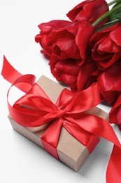Photo of Beautiful gift box with bow and red tulip flowers on white background, closeup