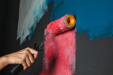 Photo of Woman painting grey wall with pink dye, closeup