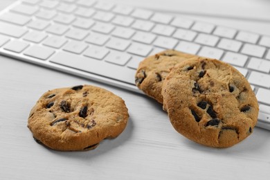 Photo of Chocolate chip cookies and keyboard on white wooden table, closeup