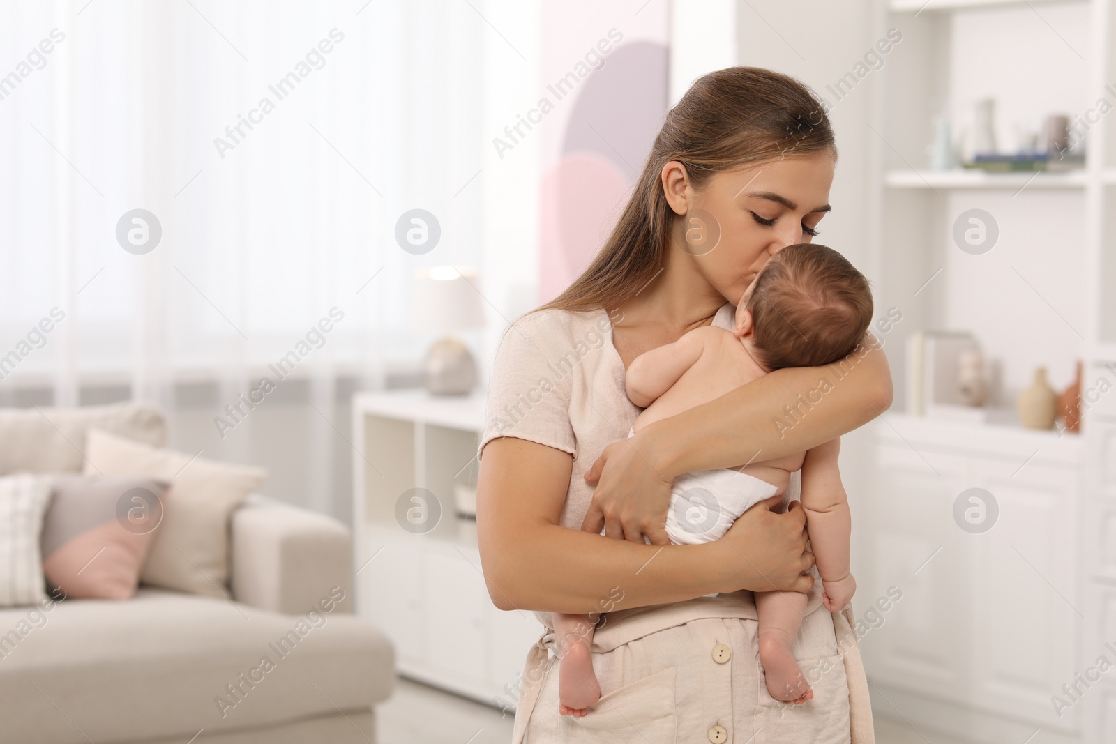 Photo of Mother kissing her cute newborn baby at home, space for text