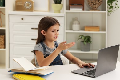 Photo of Cute girl using laptop at white table indoors