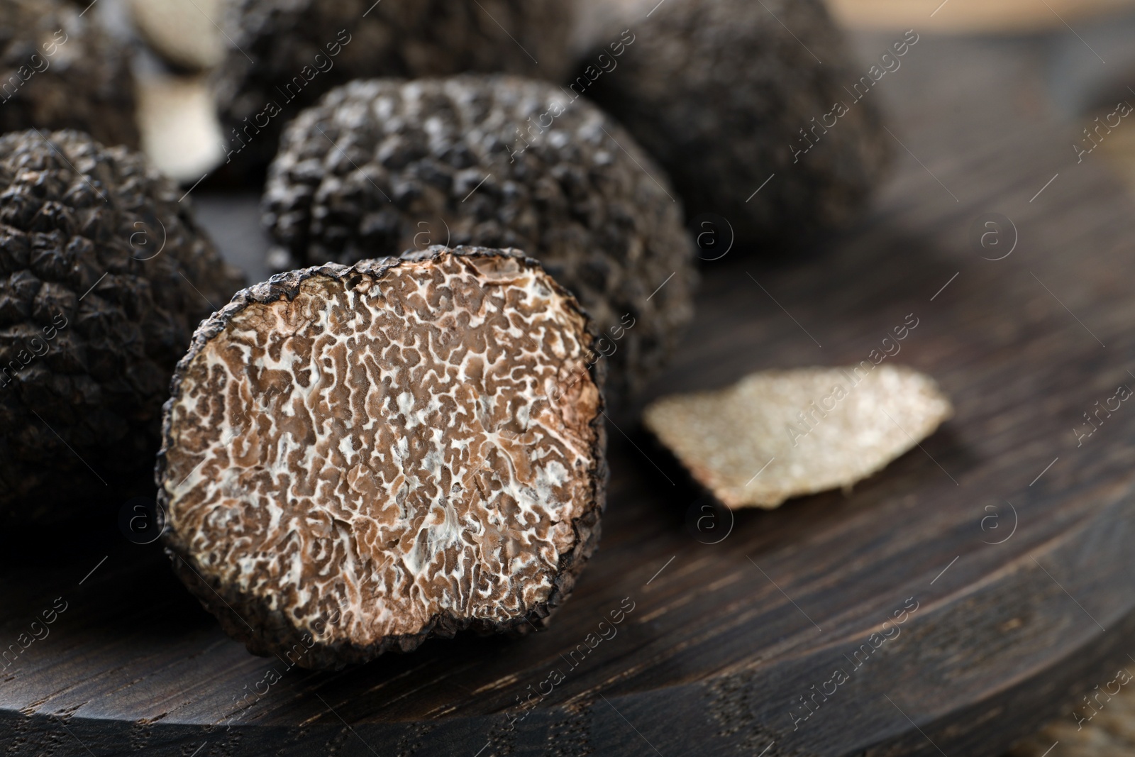 Photo of Whole and cut black truffles on wooden board, closeup