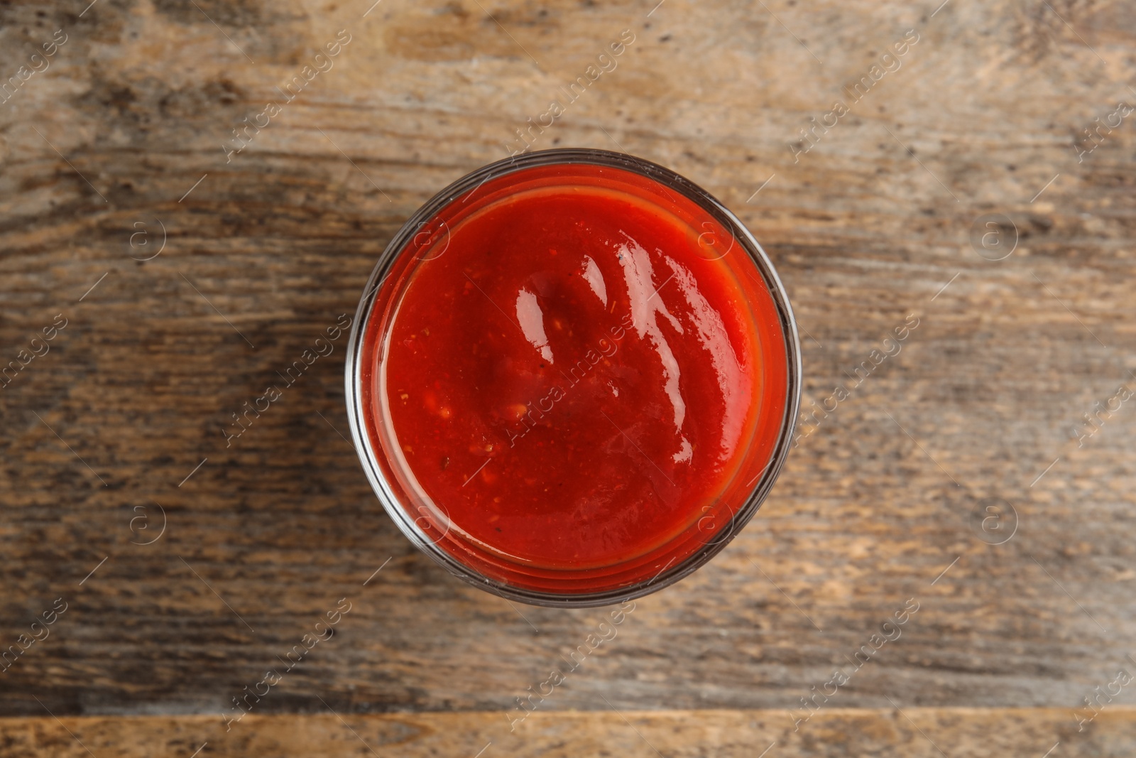 Photo of Glass of tasty tomato sauce on wooden table, top view