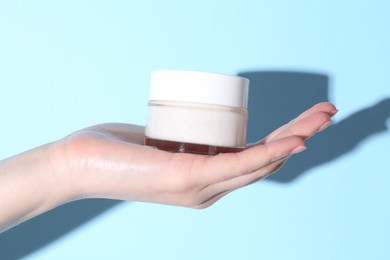 Woman holding jar of cream on light blue background, closeup