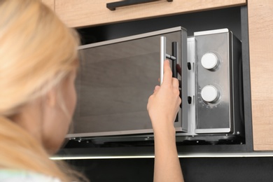 Photo of Young woman using microwave oven in kitchen, closeup