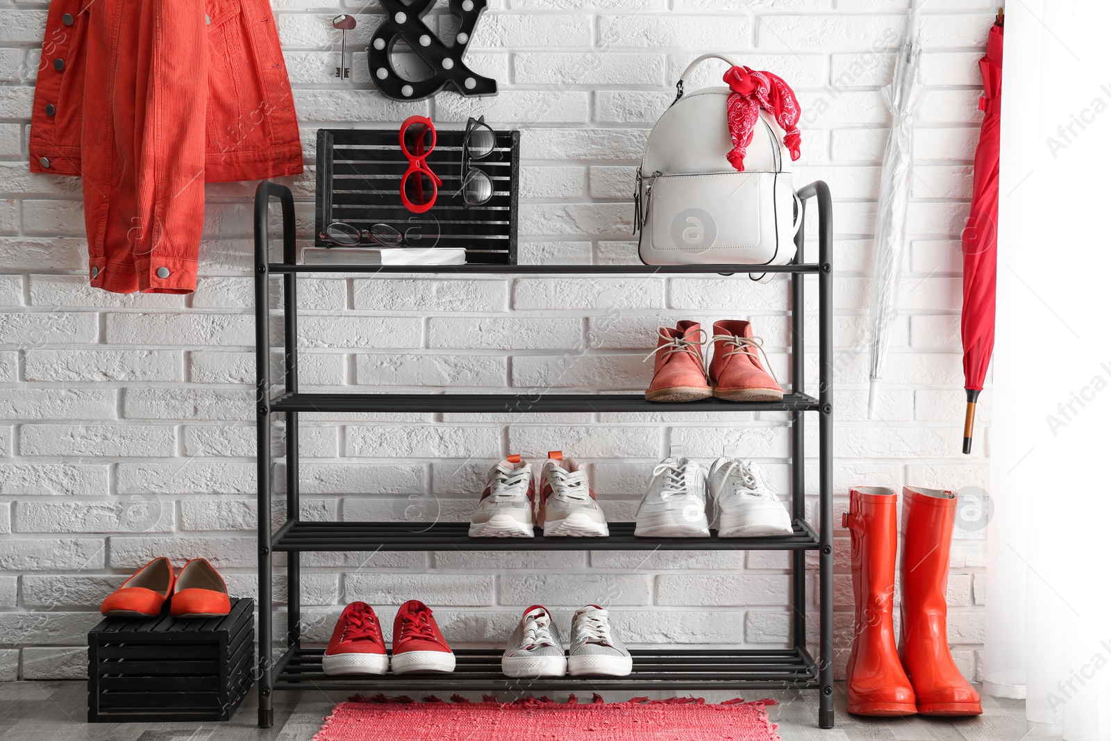 Photo of Shelving rack with stylish women's shoes and accessories near white brick wall indoors