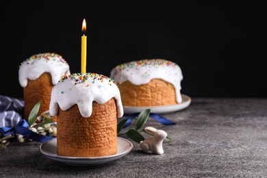 Photo of Traditional Easter cakes and one with burning candle on grey table against black background. Space for text