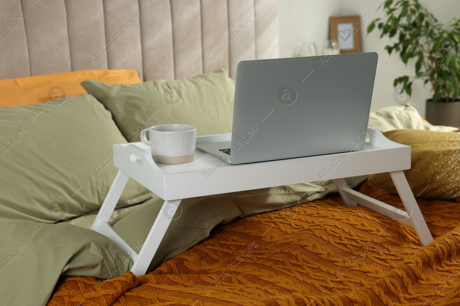 Photo of White tray with modern laptop and cup of aromatic drink on bed indoors