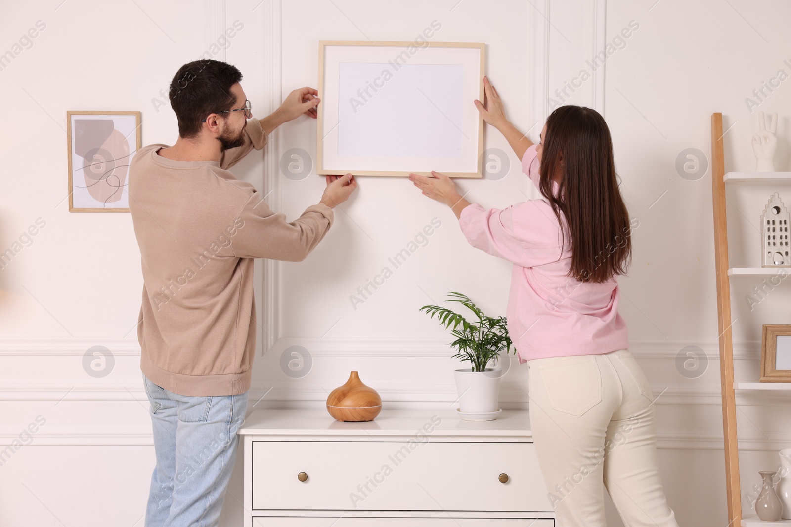 Photo of Man and woman hanging picture frame on white wall at home