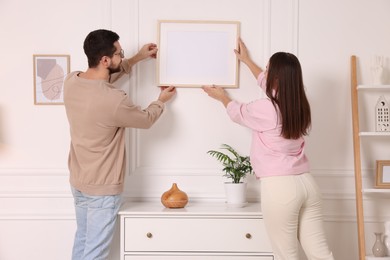 Man and woman hanging picture frame on white wall at home