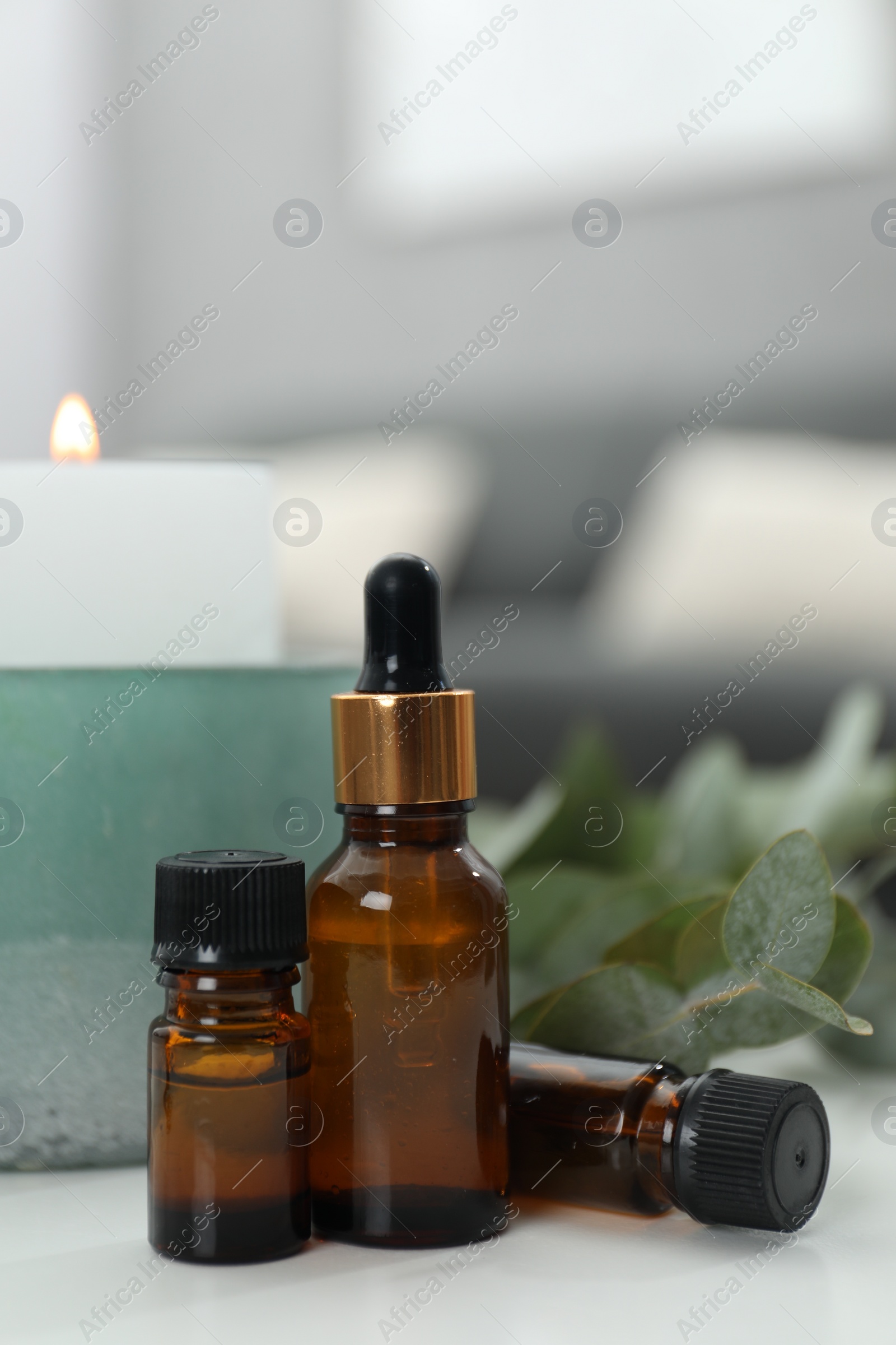 Photo of Aromatherapy. Bottles of essential oil, burning candle and eucalyptus leaves on white table