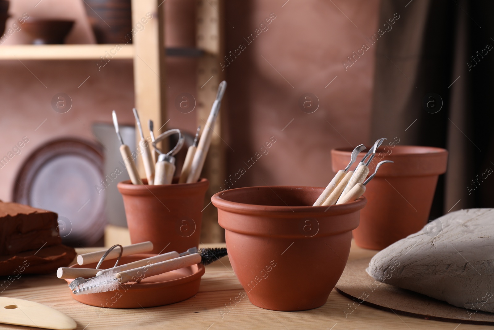 Photo of Set of different clay crafting tools on wooden table in workshop