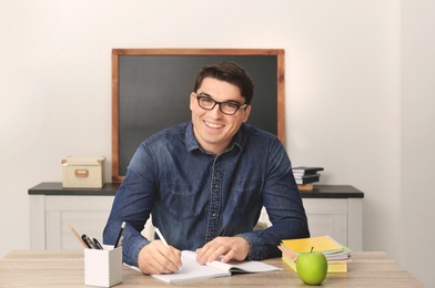 Photo of Portrait of male teacher sitting at table in classroom