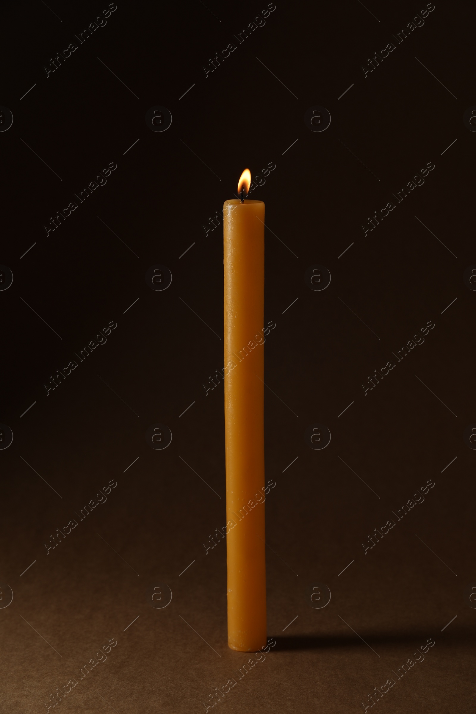 Photo of Burning church wax candle on dark background