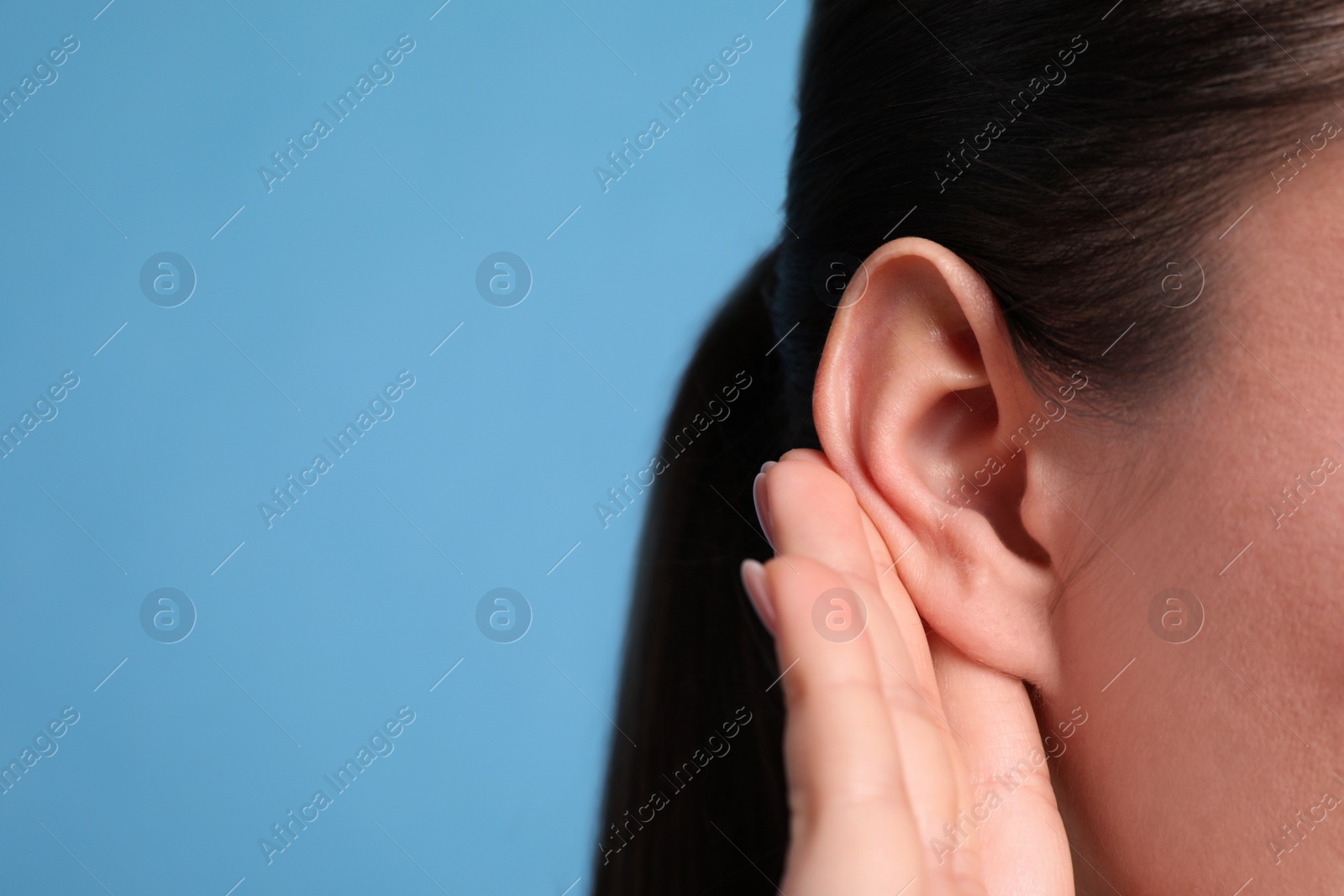 Photo of Young woman showing hand to ear gesture on light blue background, closeup. Space for text