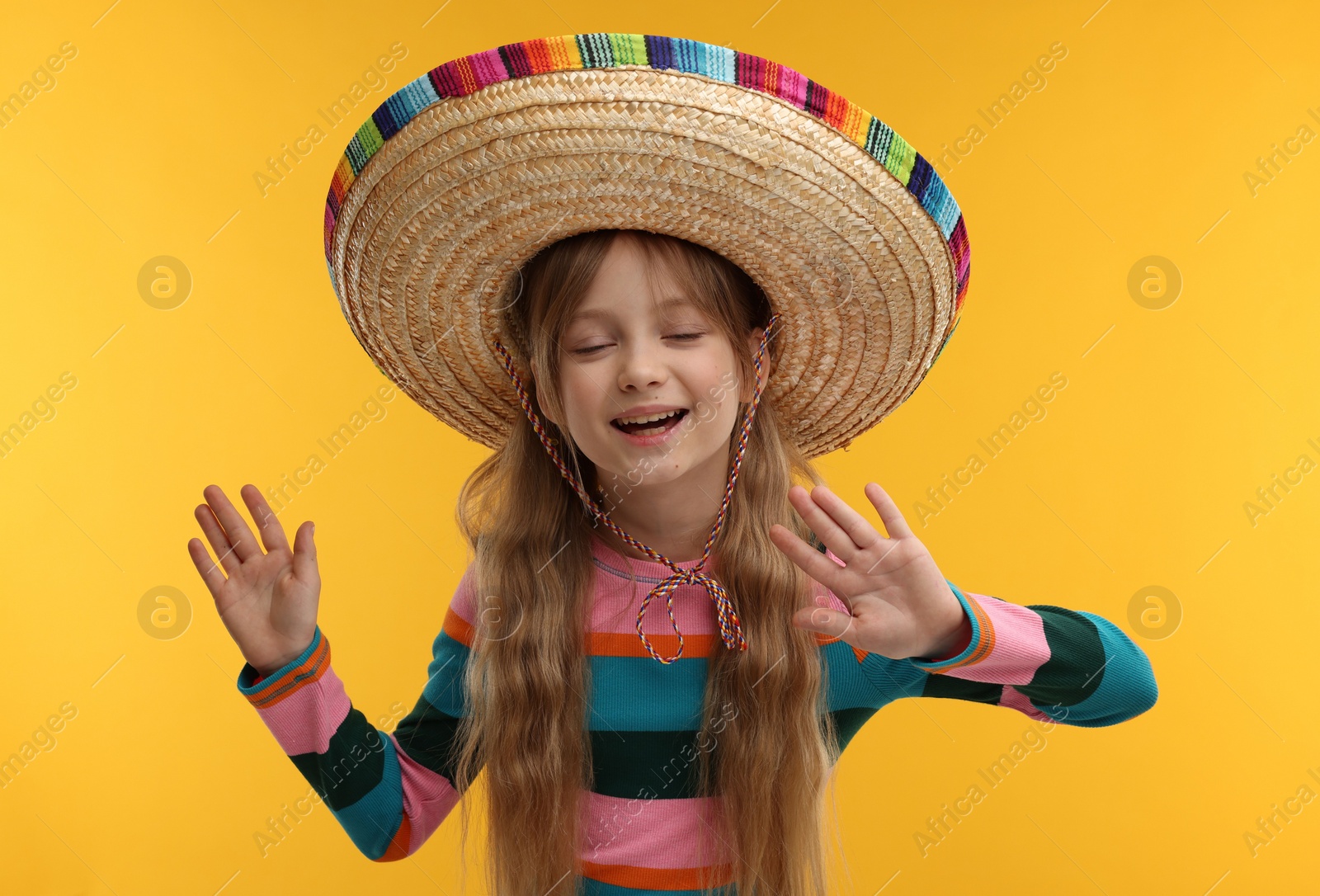 Photo of Cute girl in Mexican sombrero hat on orange background