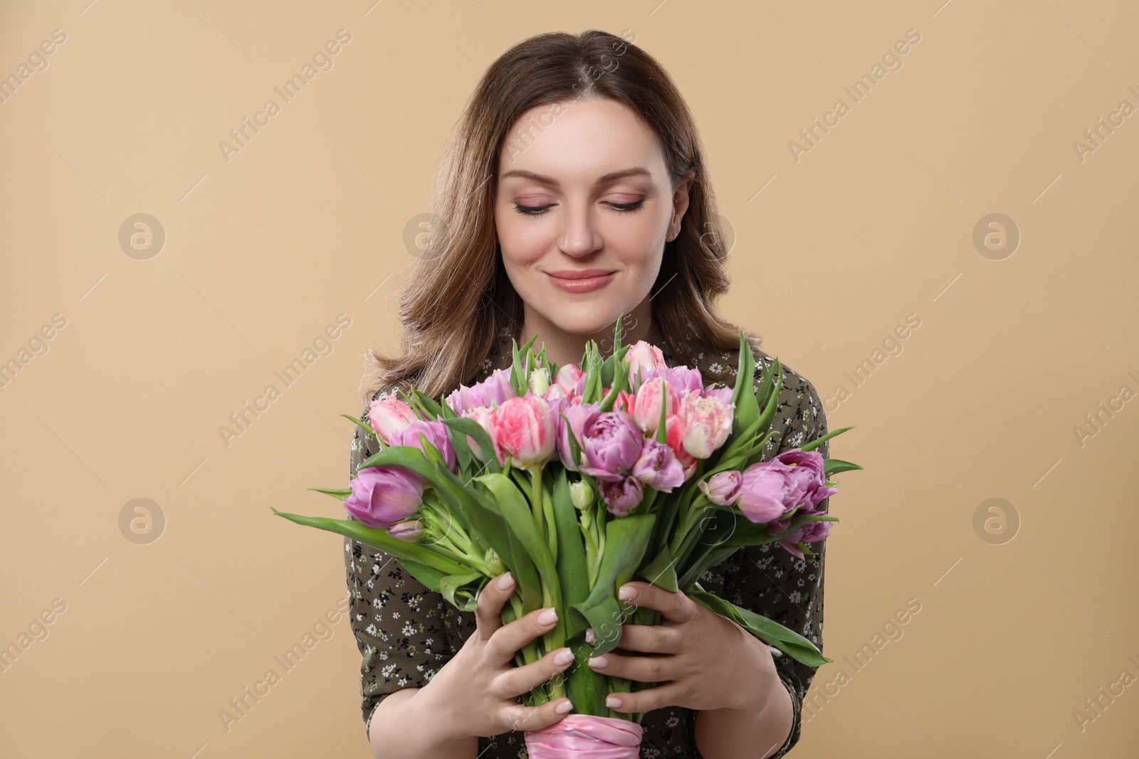 Photo of Happy young woman holding bouquet of beautiful tulips on beige background