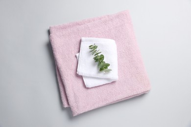 Photo of Soft folded towels with eucalyptus branch on light grey background, top view