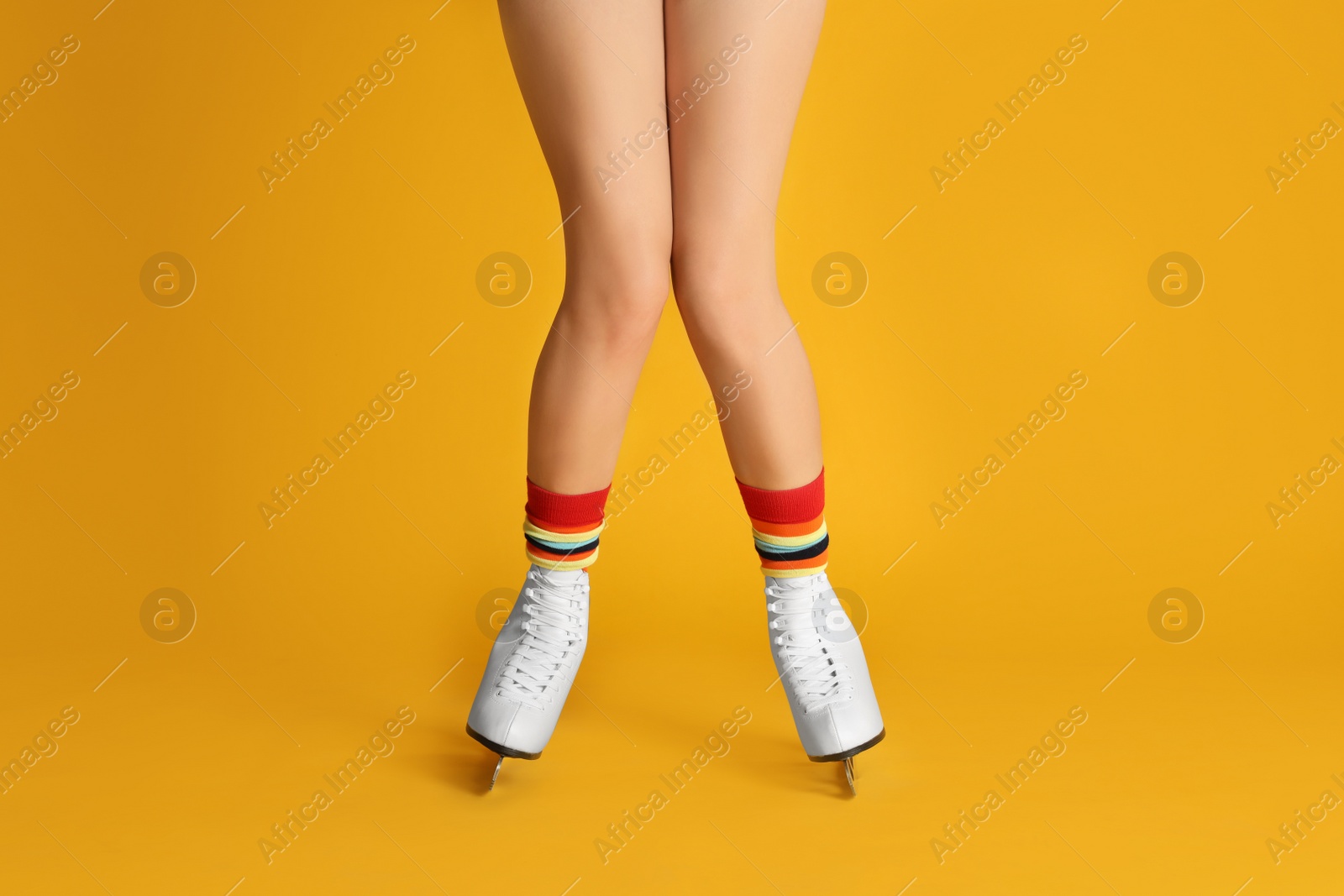Photo of Woman in elegant white ice skates on yellow background, closeup of legs
